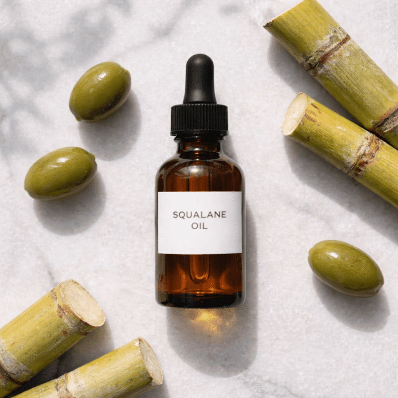 Amber dropper bottle of squalane oil with olives and sugarcane on marble surface
