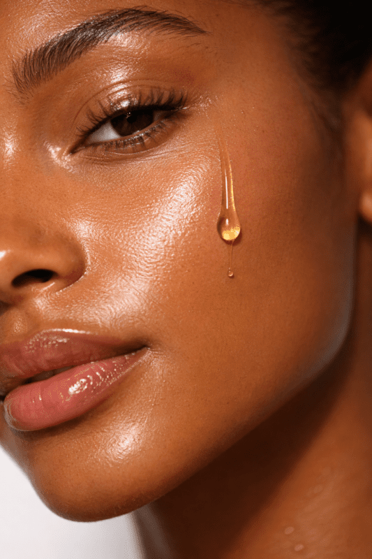 Woman with dewy glowing brown skin with a drop of squalane facial oil