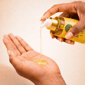"SKC’Jumira Body Oil being dispensed from a gold pump bottle into an open palm, showing the texture of the oil."
