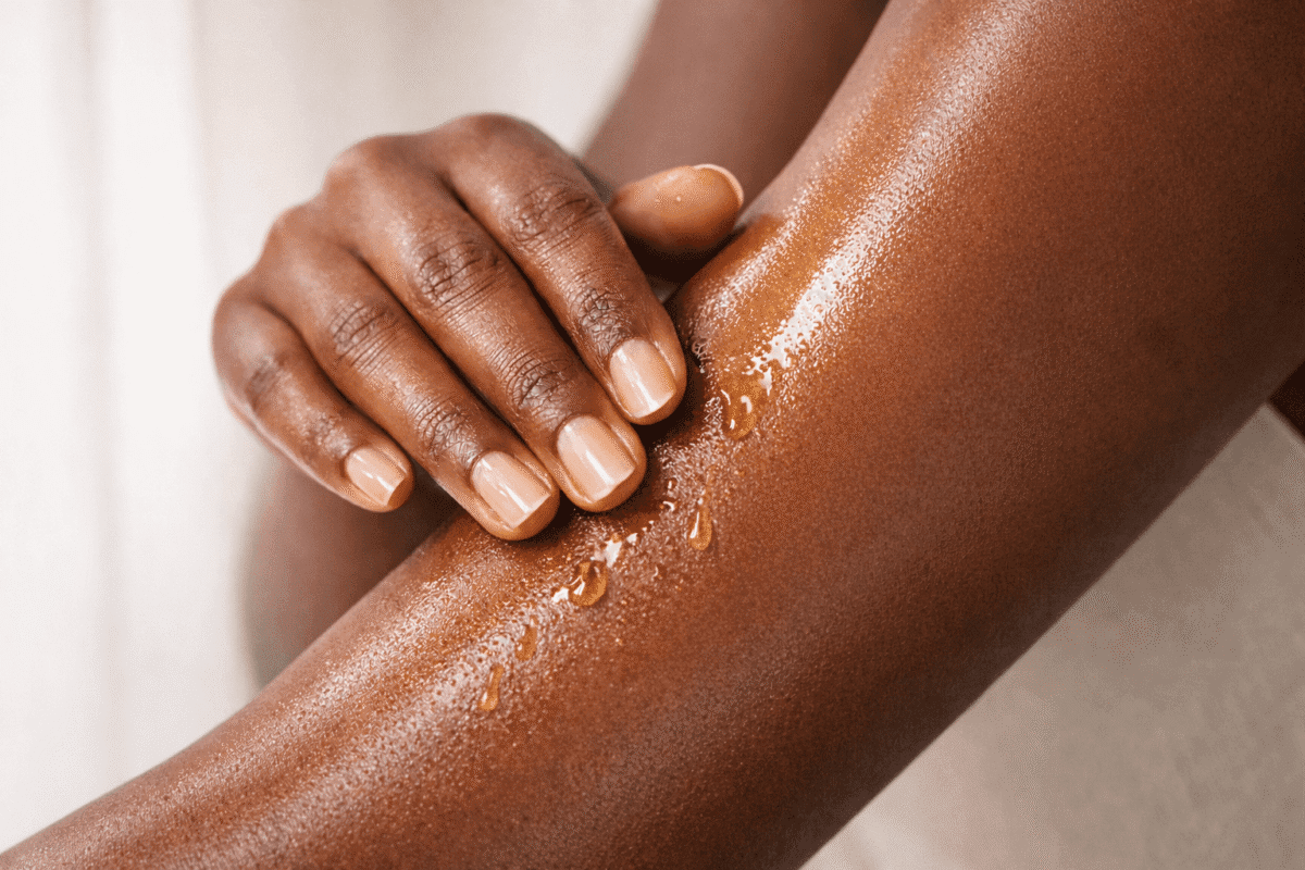 Dark-skinned woman applying squalane body oil to forearm — how to use body oil on Nigerian skin